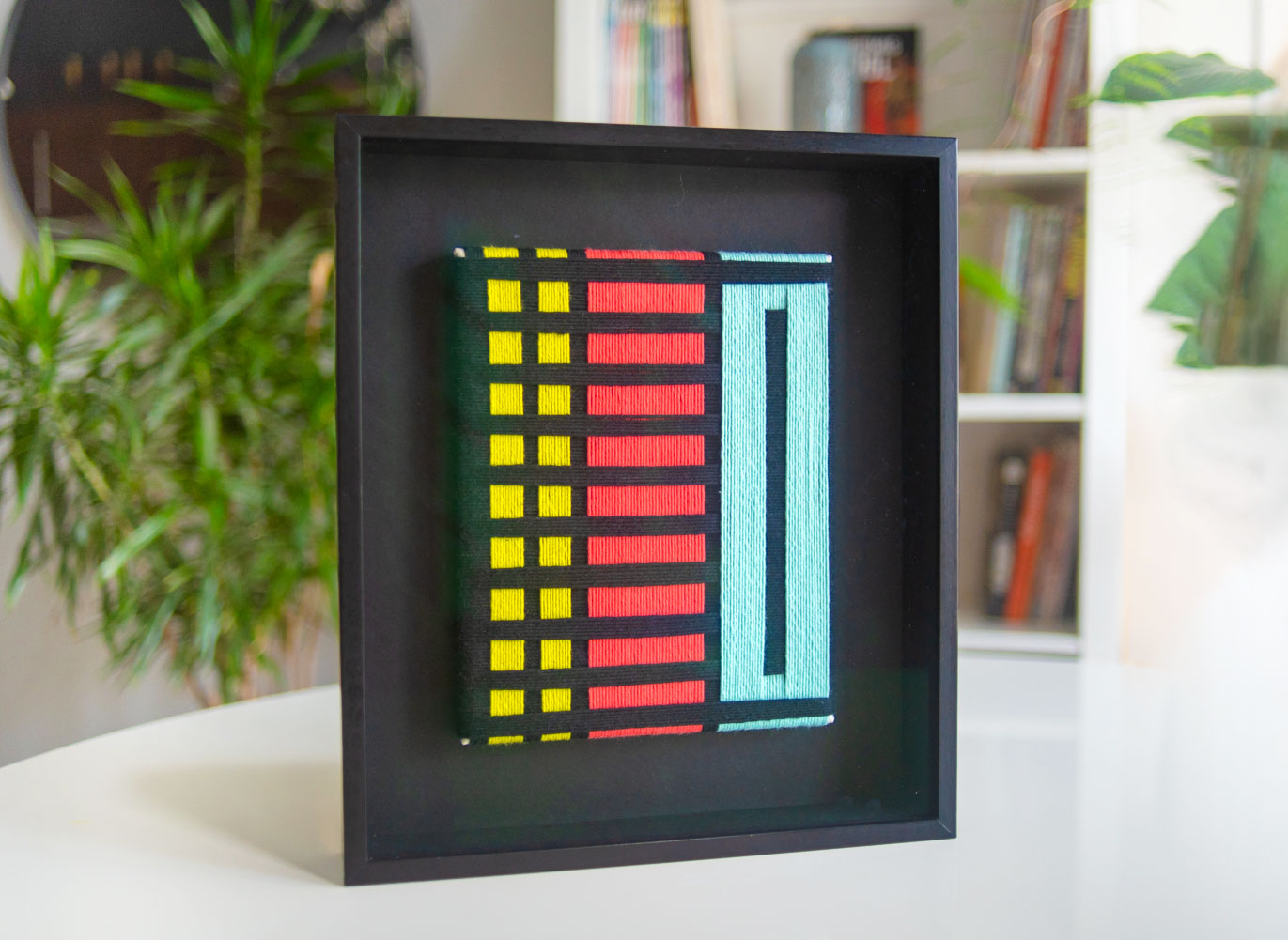 Framed textile artwork with colorful geometric design.
