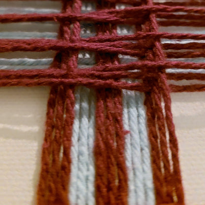 Close-up of a woven textile art showing dark red and light blue horizontal stripes with dark red vertical yarn.