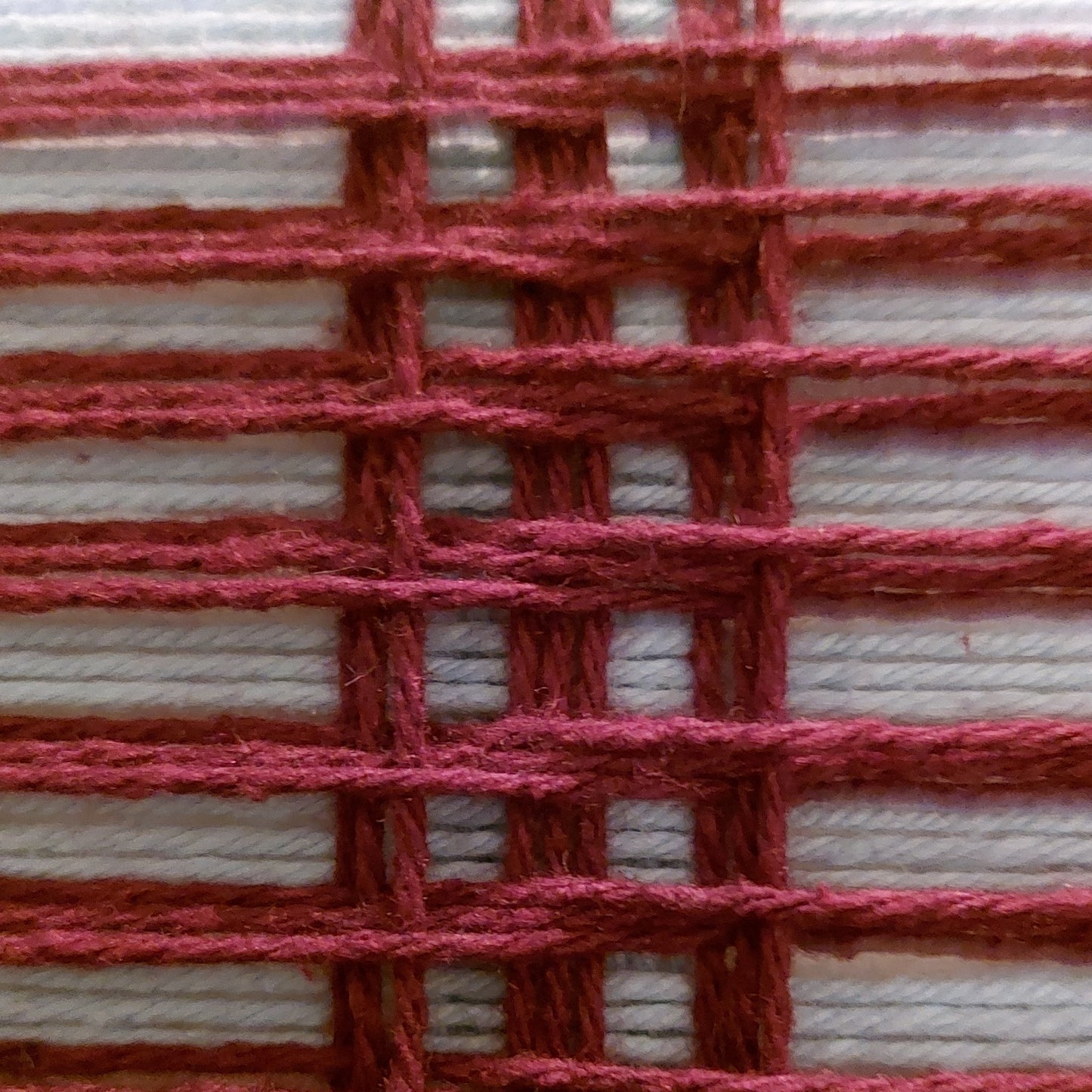 A close-up of a woven textile pattern showing dark red yarn interlaced with light blue yarn in a basketweave arrangement.