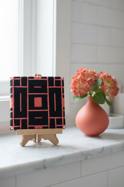 Textile art - Black and coral woven pattern on a white background