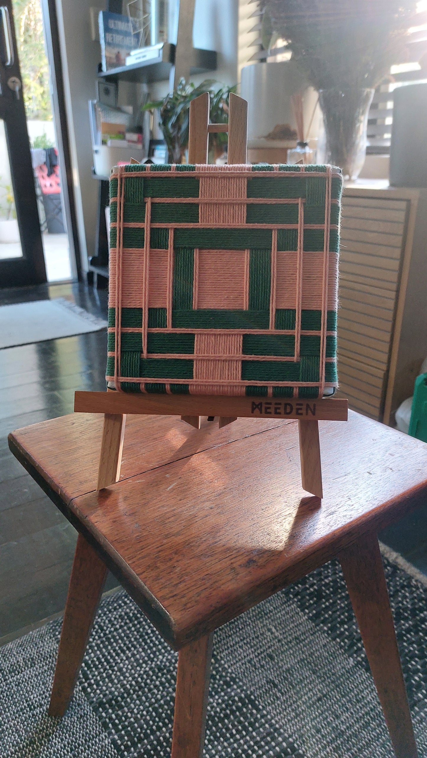 Small textile art on a wooden easel with a geometric design, placed on a table indoors.