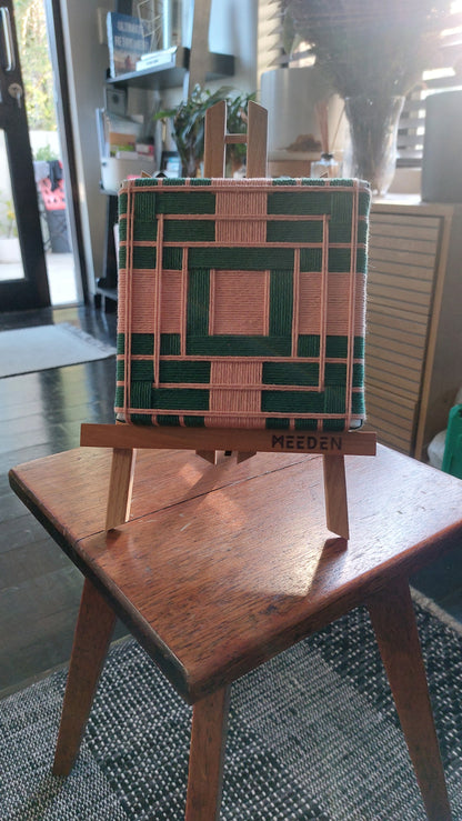 Small textile art on a wooden easel with a geometric design, placed on a table indoors.