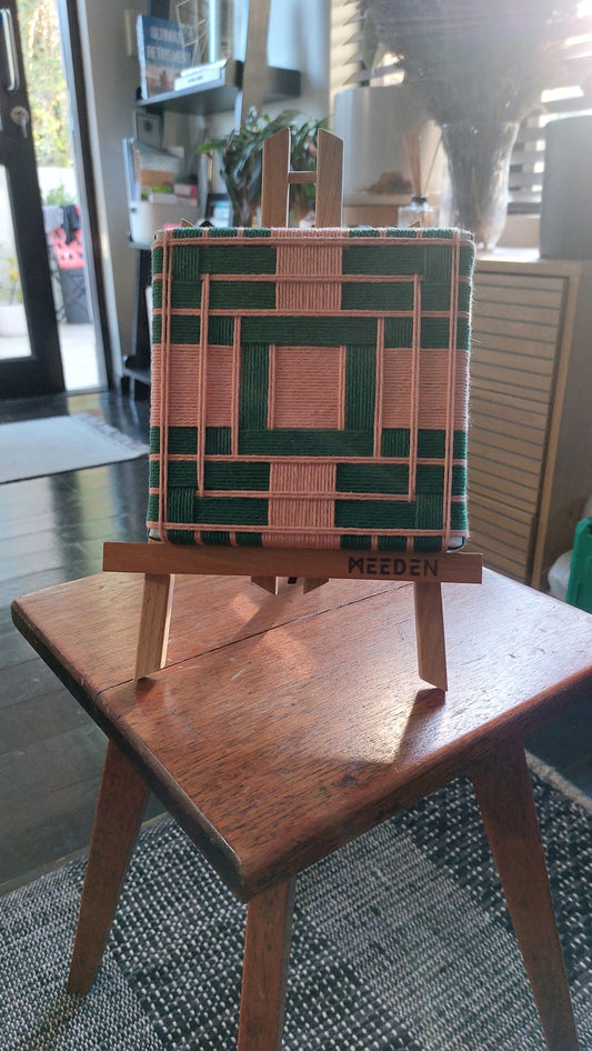 Small textile art on a wooden easel with a geometric design, placed on a table indoors.